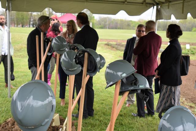 shovels and hats at groundbreaking with people in the background standing under a large tent